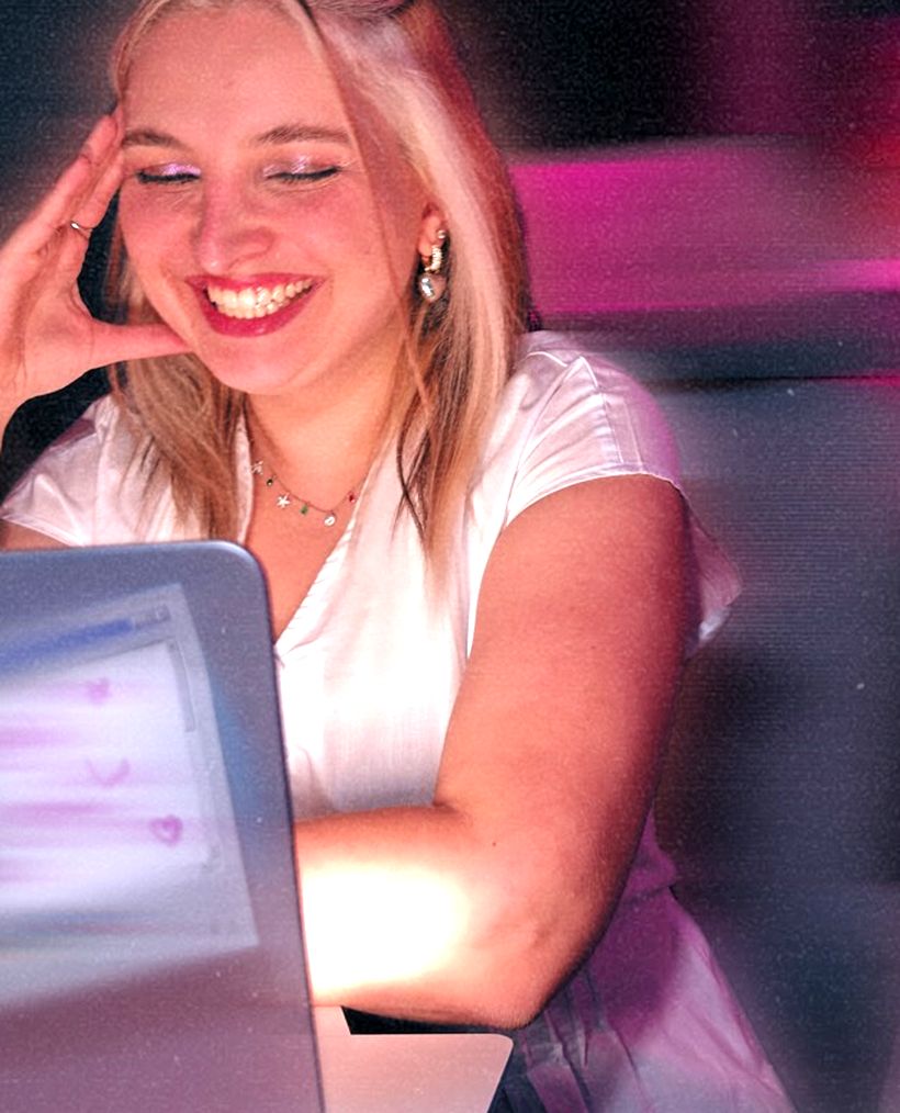Mourize rindo na frente do computador, com luz rosa ao redor